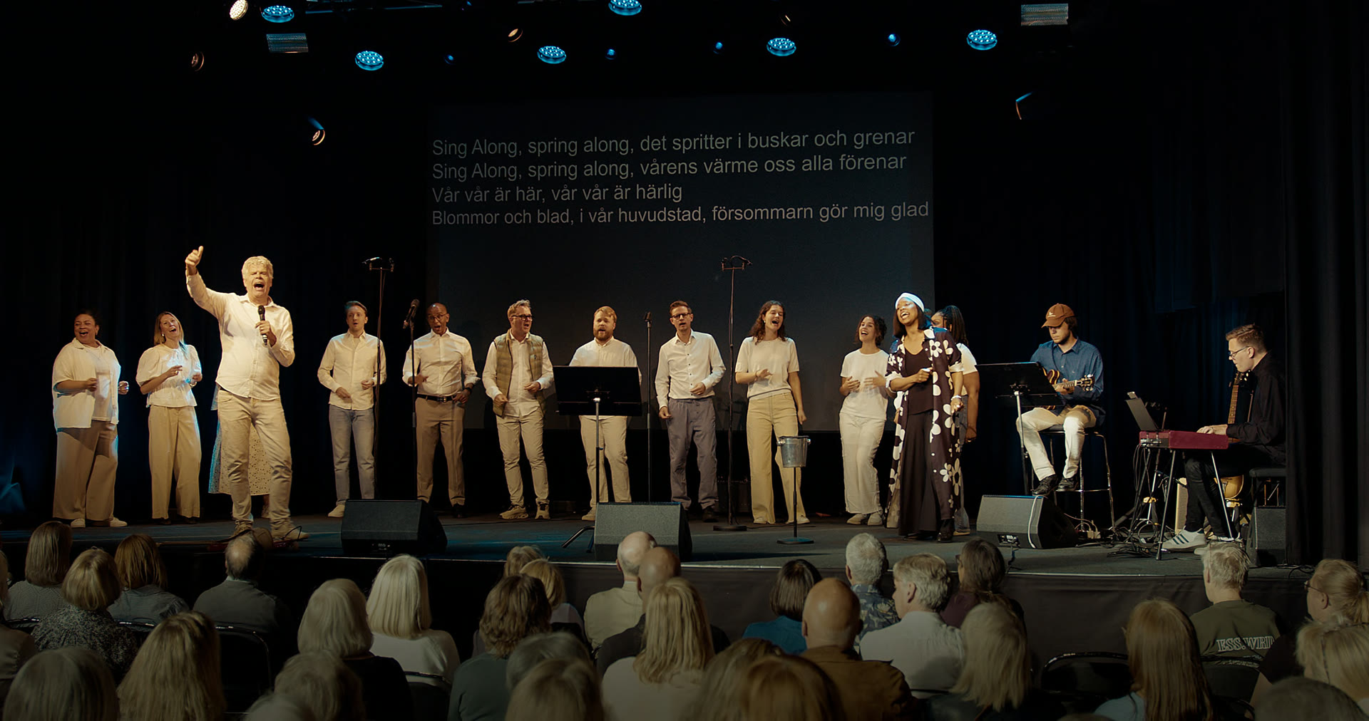 Kör och publik sjunger tillsammans på scen i blått scenljus